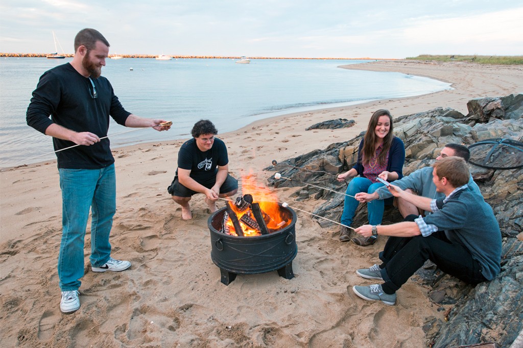 Several students sitting on the beach and having a bonfire