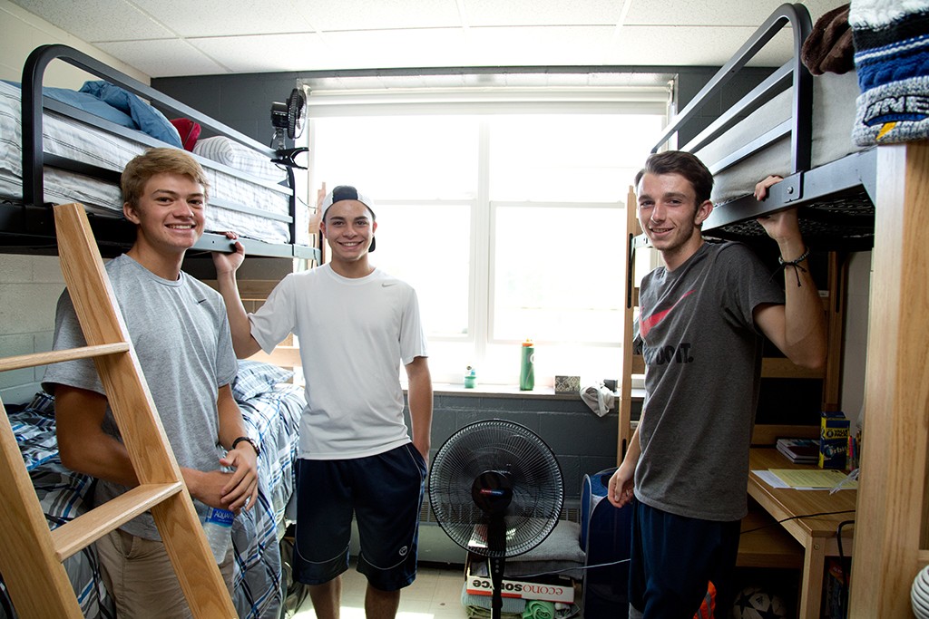 Three U N E students stand near their bunk beds in a dorm room