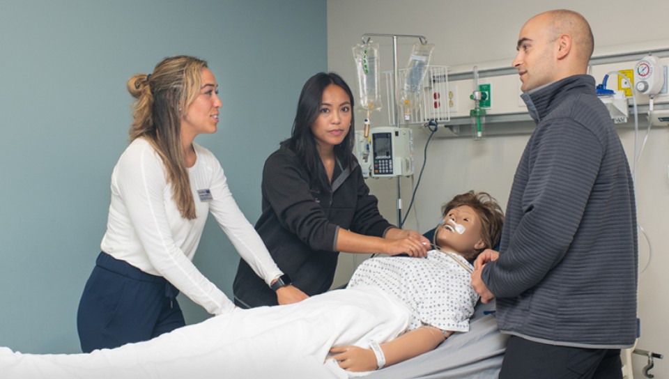 Three physical therapy students practicing on a dummy in the Simulation Lab