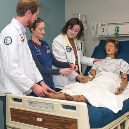 Three U N E students from different health majors work together on a dummy in the Simulation Lab