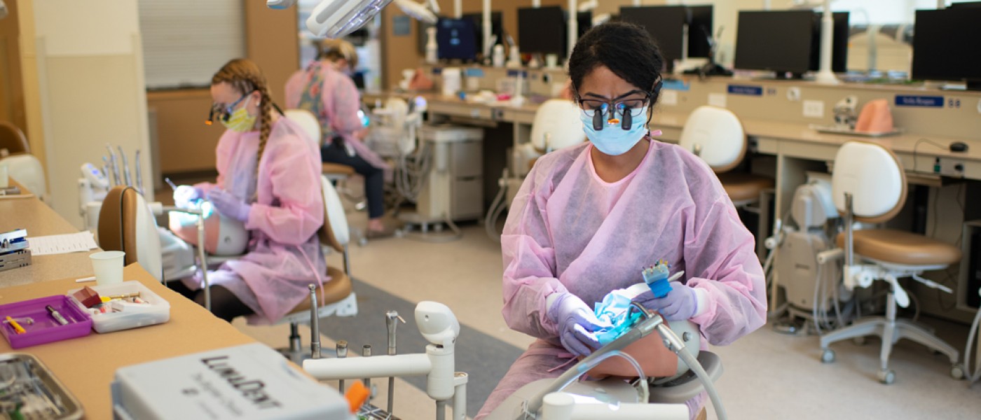 U N E dental students wearing scrubs perform oral exams on patient simulators