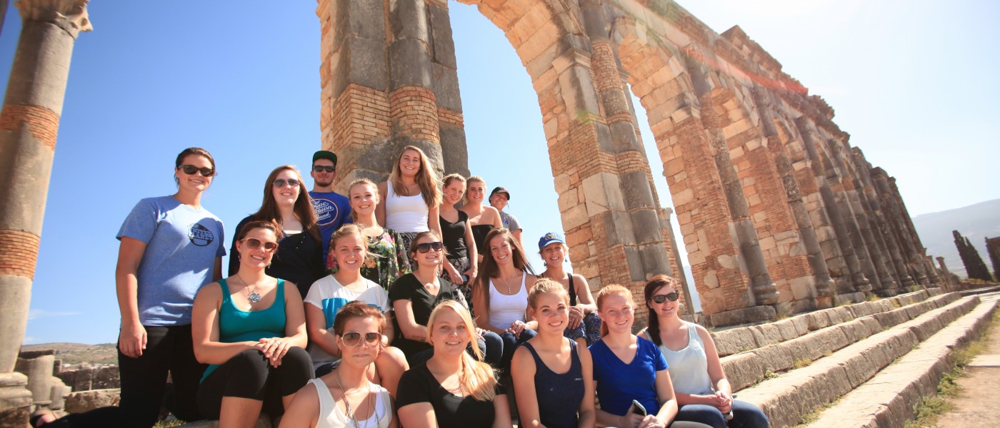 A group of U N E students sit on the steps by column ruins in Morocco