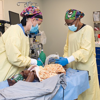 Two U N E nurse anesthesia students practicing on a child dummy